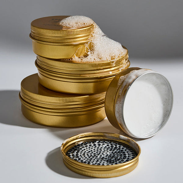 Stack of gold soap containers with different contents on a light grey background